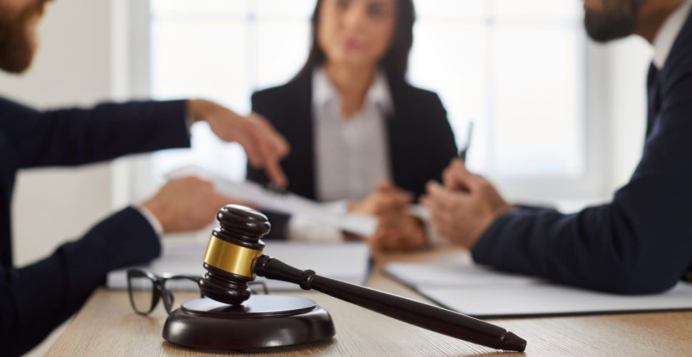 Close up of judge's gavel on desk, with lawyer or attorney meeting with group of angry complaining clients in background, giving legal consultation, helping with problem in court. Law services concept